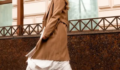 girl in brown coat and beige dress is spinning in the street