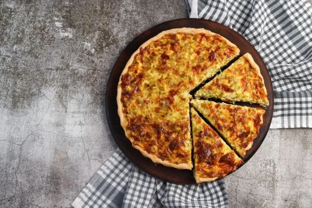 Leek and cheese pie on a round wooden cutting board on a dark grey background. Top view, flat lay